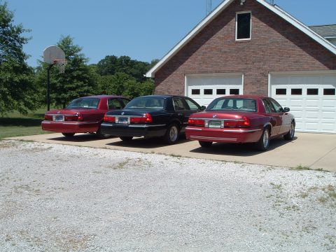 2001 Mercury Grand Marquis - Three Mercury Grand Marquis sedans are parked in front of a brick garage with white doors.