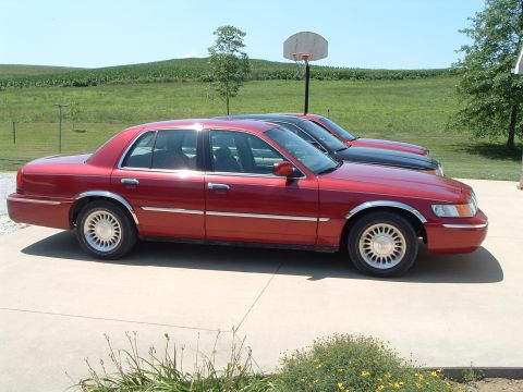 2001 Mercury Grand Marquis - A red 2001 Mercury Grand Marquis sedan is parked next to another vehicle on a sunny day.