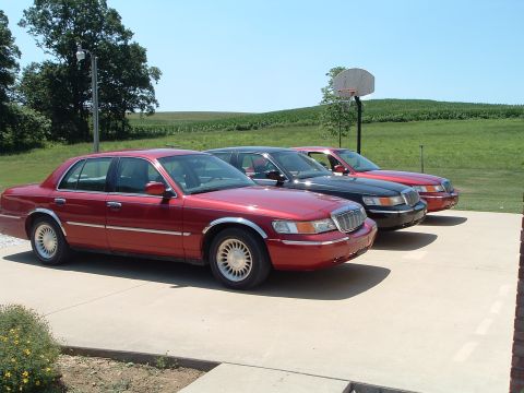 2001 Mercury Grand Marquis - Three Mercury Grand Marquis sedans are parked in a line on a sunny day with a field in the background.