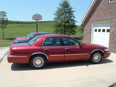2001 Mercury Grand Marquis - A red sedan is parked in front of a garage, with another vehicle visible behind it.