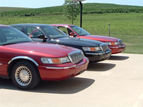 2001 Mercury Grand Marquis - Three Mercury Grand Marquis sedans are lined up on a concrete driveway with a grassy hill in the background.