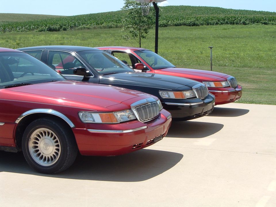 Three Mercury Grand Marquis sedans parked in a row, red, black, and red