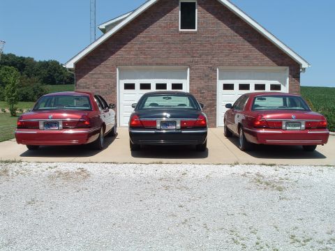 2001 Mercury Grand Marquis - Three Mercury Grand Marquis sedans are parked in front of a two-car garage on a sunny day.