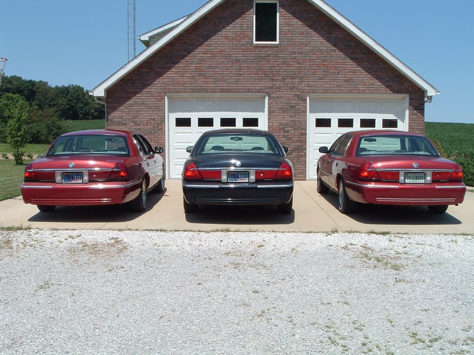 Three 2001 Mercury Grand Marquis sedans parked in front of a brick garage with white doors