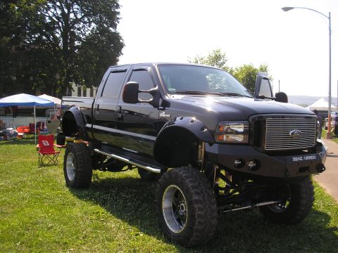 1995 Ford Bronco - A heavily modified black Ford F-250 Super Duty truck is displayed outdoors on a sunny day.