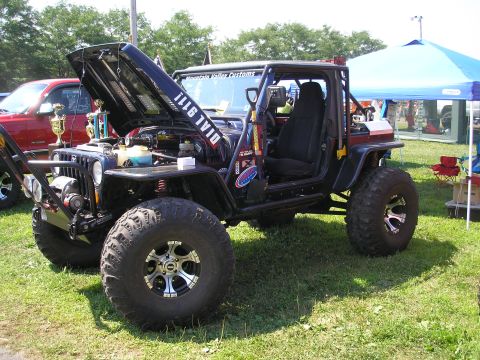 1995 Ford Bronco - A heavily modified black Jeep Wrangler is displayed with its hood open, custom off-road modifications.