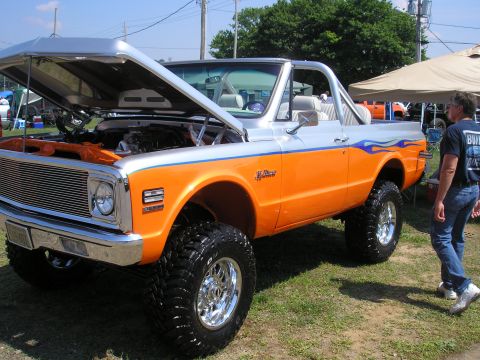 1995 Ford Bronco - This lifted SUV features a two-tone orange and silver paint scheme with flame decals and its hood is open, revealing the engine.