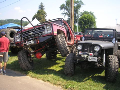 1995 Ford Bronco - Two heavily modified off-road vehicles are parked on grass under a sunny sky.