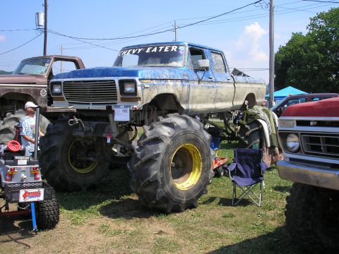 1995 Ford Bronco - A lifted blue pickup truck, modified with massive tires, sits on display next to other vehicles.