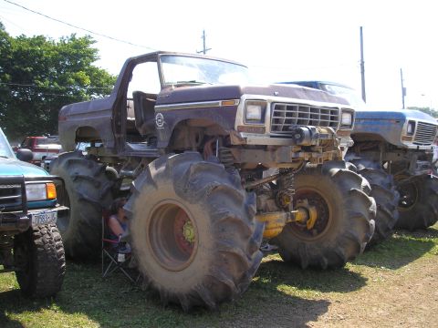 1995 Ford Bronco - A modified brown truck with oversized tires sits next to another vehicle under a bright sky.