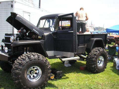 1995 Ford Bronco - A heavily modified Jeep pickup truck is displayed with its hood open, showing off its engine and large tires.