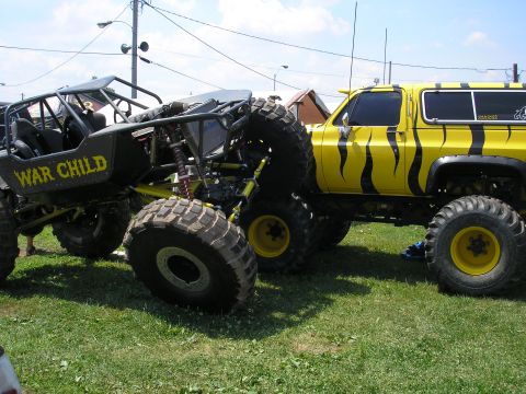 1995 Ford Bronco - Two heavily modified off-road vehicles, one a custom buggy and the other a lifted truck with tiger stripes, parked on grass.