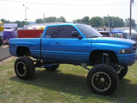 1995 Ford Bronco - A lifted blue pickup truck with custom wheels sits on a grassy field.