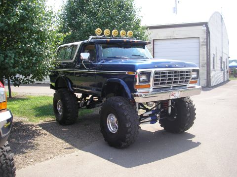 1995 Ford Bronco - A lifted blue Ford Bronco with custom lights sits parked in front of a garage.