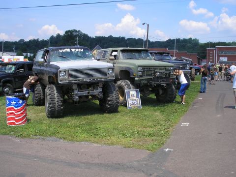 1995 Ford Bronco - Two heavily modified trucks are parked on grass, with people milling around in the background.