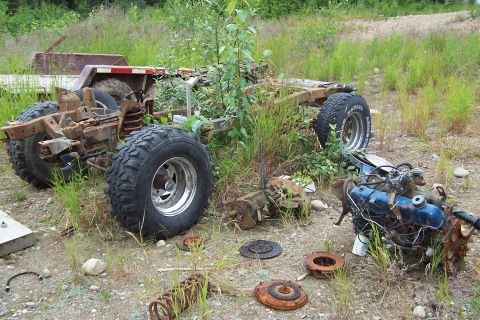 1989 Ford Bronco II - Disassembled vehicle frame and engine components lie in a grassy, overgrown area.