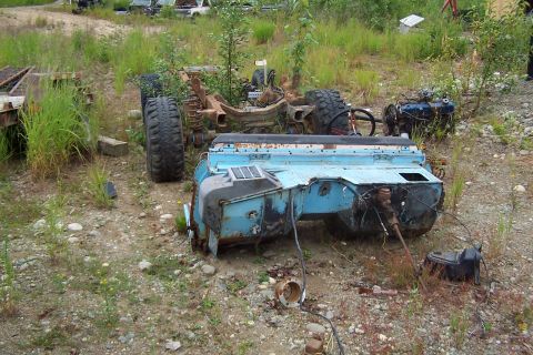 1989 Ford Bronco II - A disassembled vehicle, likely a truck or SUV, lies in pieces in an outdoor junkyard setting with overgrown grass.