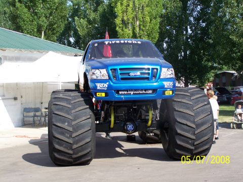 1973 Ford Mustang - A bright blue Bigfoot monster truck with massive tires is parked outdoors on a sunny day. The truck has "Firestone" and "BDS Racing" brandi…