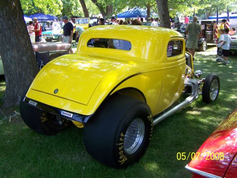 1973 Ford Mustang - A bright yellow hot rod coupe is parked on a grassy lawn with trees in the background. The rear of the vehicle features large drag racing t…