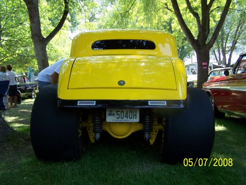 1973 Ford Mustang - The rear view of a bright yellow hot rod with oversized rear tires is shown parked on grass under trees. A license plate reading "5040H VIN…