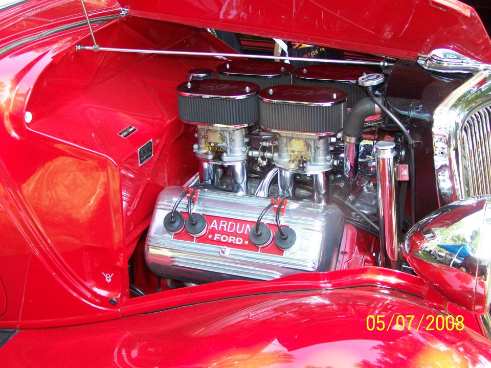 Red classic Ford V8 engine with dual carburetors and chrome air cleaners. "ARDUN FORD" text visible.