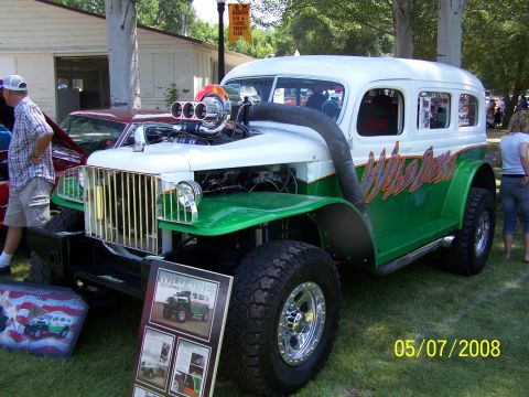 1973 Ford Mustang - A highly modified, custom green and white SUV with a large chrome exhaust pipe and a supercharger is parked on grass. A sign with photos of…