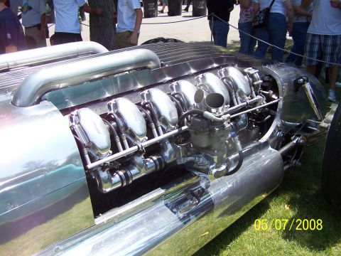 1973 Ford Mustang - A highly polished, custom engine with multiple carburetors and exhaust pipes is the focus of this image. The vehicle appears to be a classi…