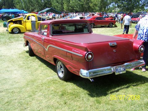 1973 Ford Mustang - The rear driver's side quarter view of a red 1957 Ford Ranchero is shown parked on a grassy field at an outdoor car show. The vehicle has a…