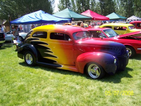 1973 Ford Mustang - A custom hot rod with a yellow, orange, red, and purple gradient paint job with black flame graphics is parked on a grassy lawn under a blu…