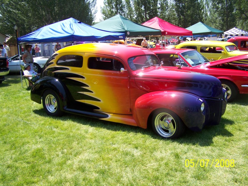 Custom hot rod with flame graphics and gradient paint job parked on grass.
