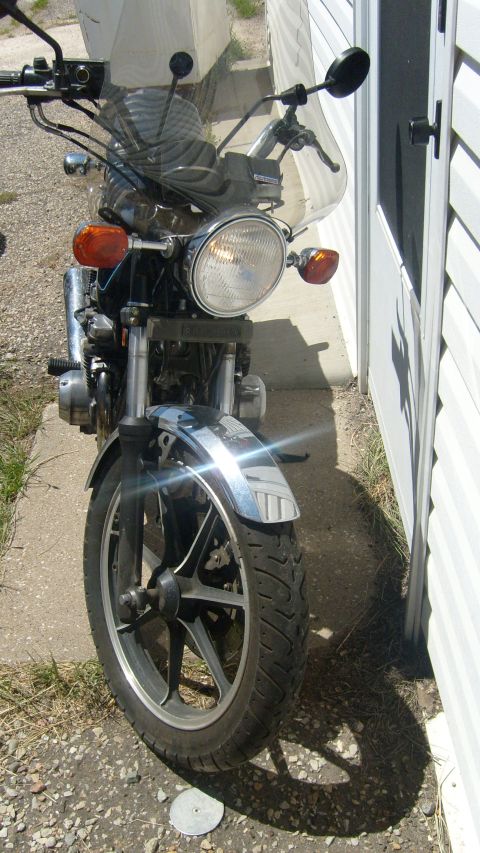 1995 Ford Bronco - The front view of a motorcycle is parked next to a white vinyl-sided building. The motorcycle has a chrome front fender and a clear windshi…