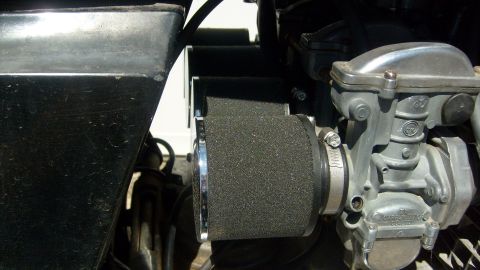 1995 Ford Bronco - A close-up view of a motorcycle carburetor with a black foam air filter attached. The shiny metal carburetor has visible branding and is co…