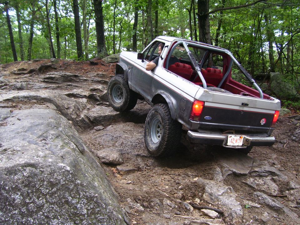 1990 Ford Ranger off-roading on a rocky, muddy trail in the woods.