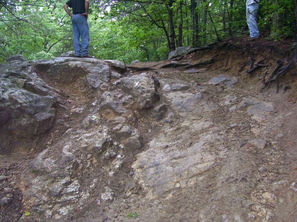 Eroded rocky off-road trail obstacle in a wooded area with two people standing