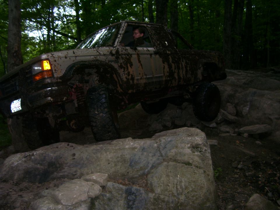 Muddy 1990 Ford Ranger off-roading over rocks in a forest.