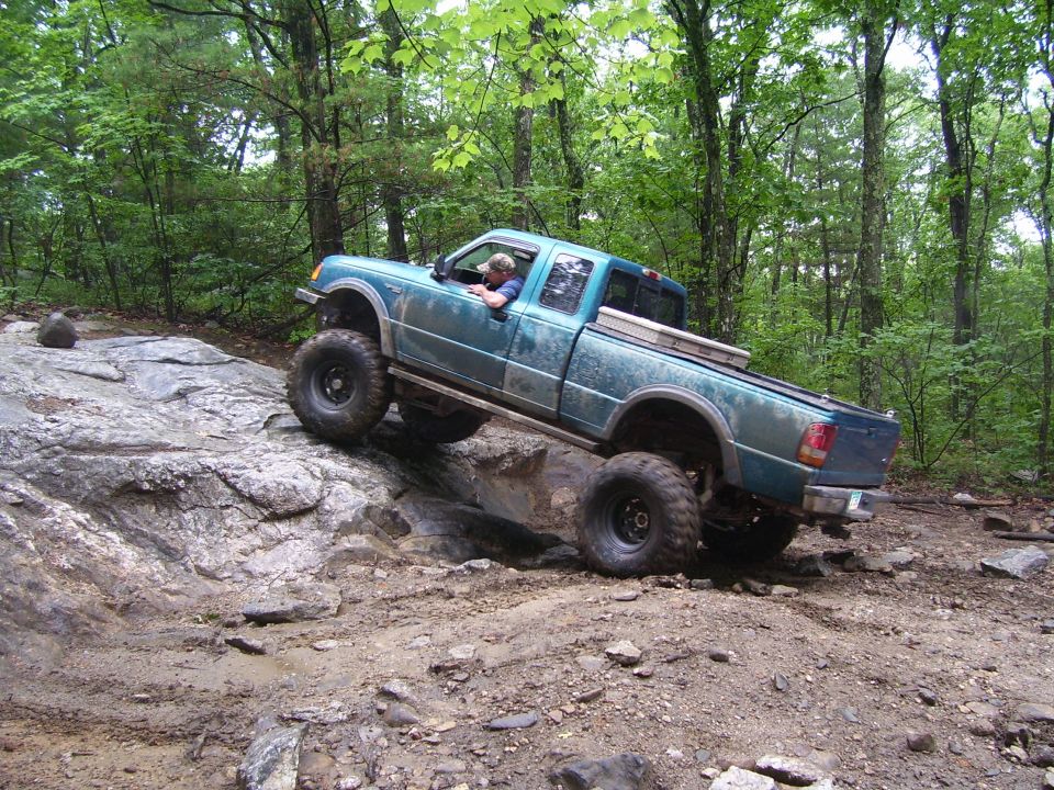 Teal Ford Ranger off-roading on a rocky, muddy trail in a forest.