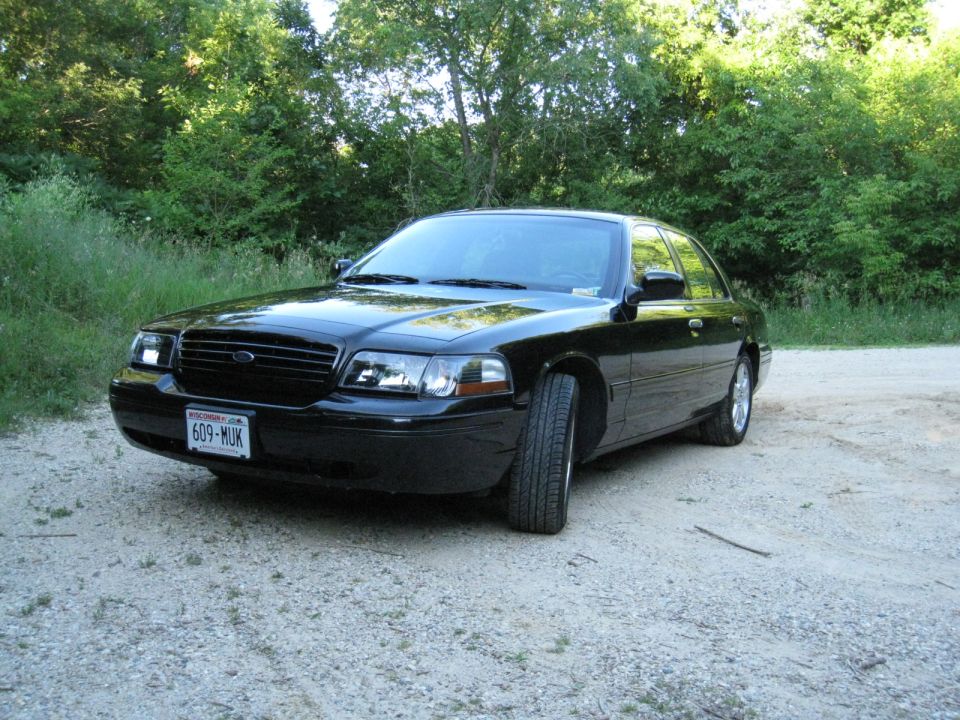 Black Ford Crown Victoria sedan parked on gravel, front view