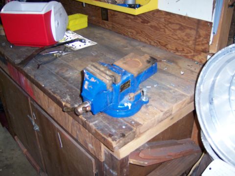 1991 Ford Bronco - Photograph of a blue bench vise clamped to a wooden workbench with a cooler and parts nearby.