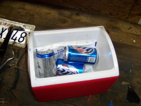 1991 Ford Bronco - Photograph of a small red cooler with drink cans on a workbench next to a license plate.