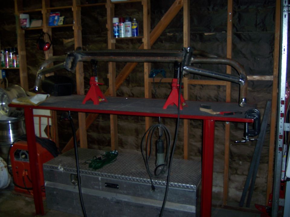 Custom front bumper assembly on red workbench with jack stands, tools, and welding equipment in garage