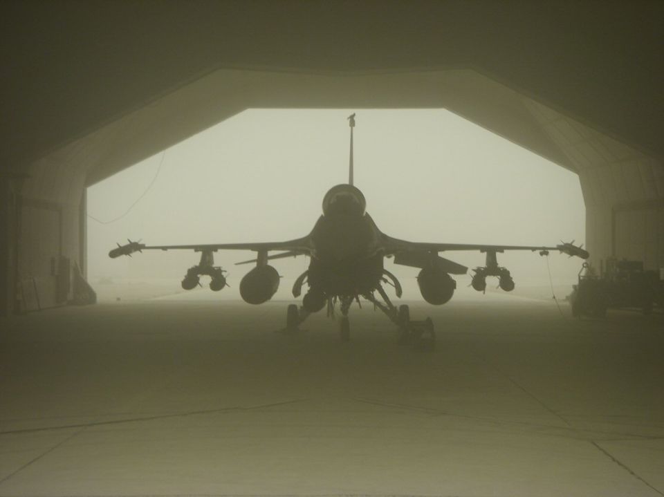 Silhouette of an F-16 fighter jet in a hardened aircraft shelter in haze