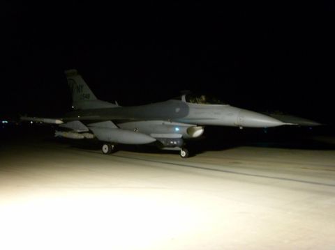 1978 Ford Bronco - A gray F-16 fighter jet is parked on a tarmac at night, illuminated by ground lights.