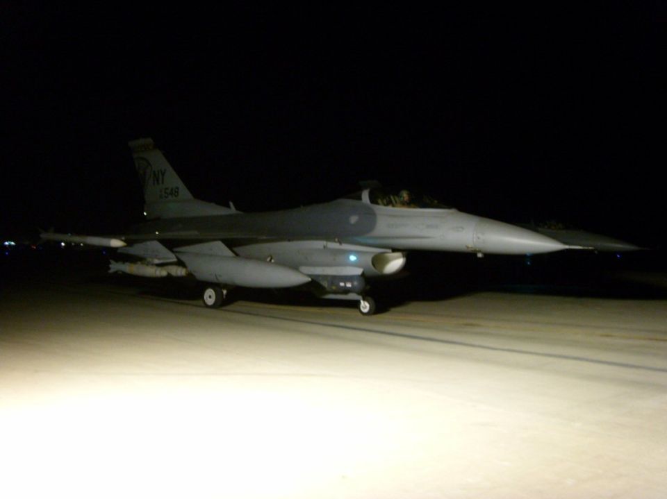 Gray F-16 fighter jet with missiles on wings, parked on tarmac at night