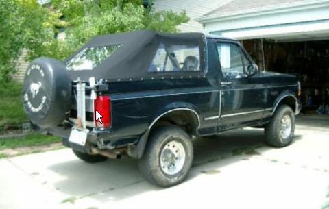 1995 Ford Bronco - This black 1995 Ford Bronco features a soft top and a rear-mounted spare tire carrier, parked in a driveway.