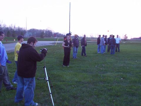 1998 Ford Taurus - A group of people are gathered in an open field, with one individual operating a video camera on a tripod.