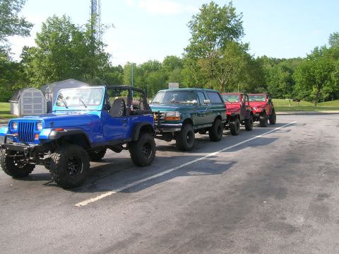 1996 Ford Bronco - A line of off-road vehicles, including a green Ford Bronco, are parked in a lot.