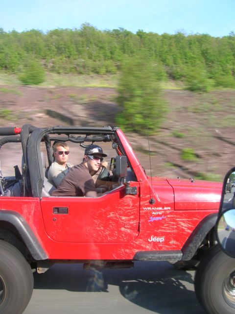 1996 Ford Bronco - A red Jeep Wrangler 4.0 Sport drives on a dirt road with two people inside.
