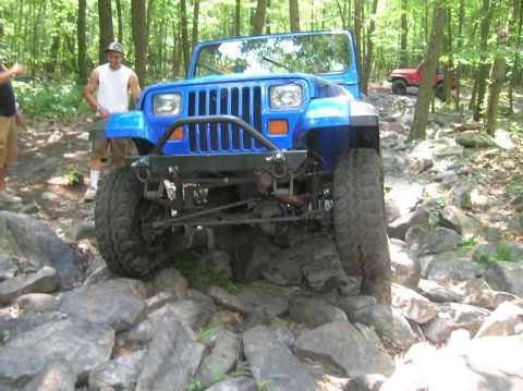 1996 Ford Bronco - A blue Jeep Wrangler navigates a challenging rocky trail with another Jeep visible in the distance.