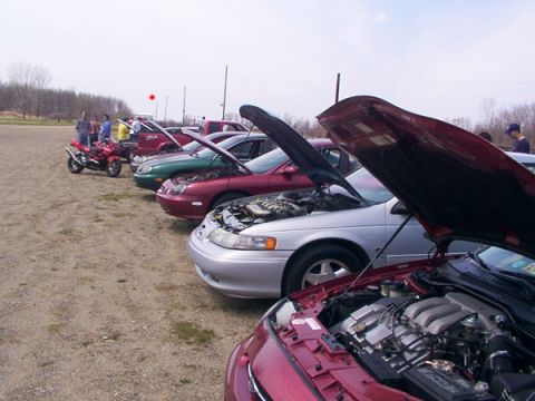 1998 Ford Taurus - Several cars and a motorcycle are parked in a lot with their hoods open, suggesting a car show or meet.