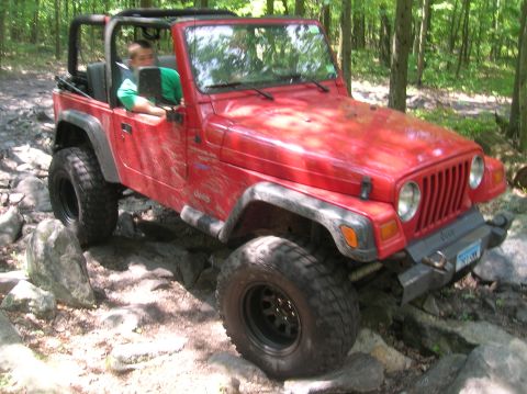 1996 Ford Bronco - Red Jeep Wrangler TJ navigating a rocky off-road trail in a forest.